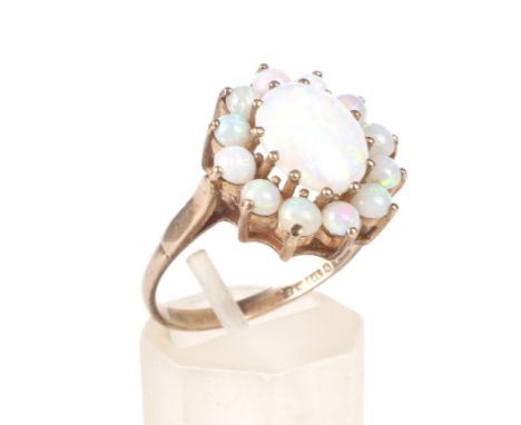 A vintage 9ct gold and white-opal oval cluster ring. Centred with an oval cabochon white opal within a small round cabochon t