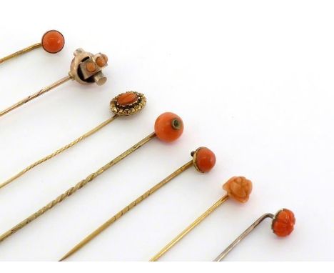 A collection of coral-mounted stickpins, including a carved coral example with a chased rocaille scroll border (tests 14 cara