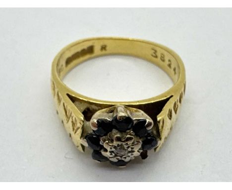An 18ct Gold Diamond and Sapphire Cluster Ring, of flowerhead design, between wide tapered shoulders of textured finish (fing