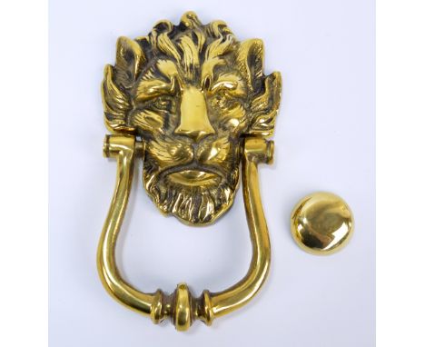 A large decorative brass door knocker in the form of a lion head mask, with brass button and three fixing screws, height 22cm