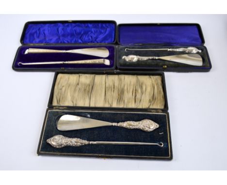 A cased George V hallmarked silver sheath handled set of button hook and shoe horn with scrolling repousse decoration, J & R 