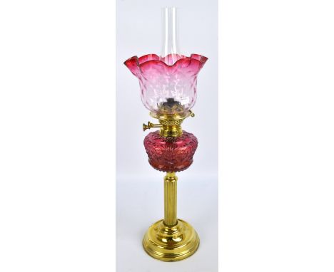 A brass oil lamp with ruby glass reservoir above fluted column stem, wick adjustors with manufacturers stamp for Duplex, heig