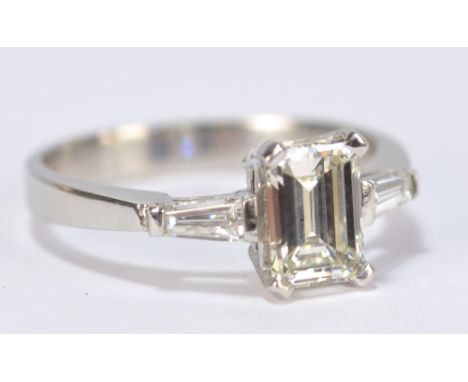 An 18ct white gold and diamond ring, the central emerald cut stone weighing 1.23ct, colour H, clarity VS1 (no fluoresence), f