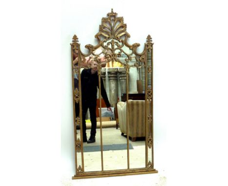 An ornate gilt framed Gothic inspired wall mirror with pierced scrolling pediment and plinth shelf, height 152cm, width 78cm.