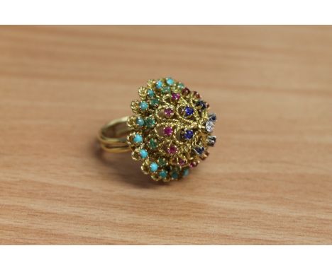 A high carat gold multi-gemstone ring, set with tiers of turquoise, emeralds, rubies, sapphires around a central brilliant cu