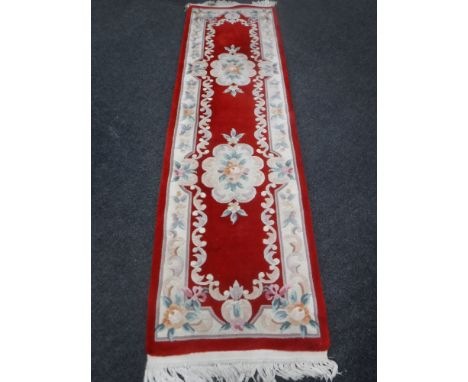 A Chinese fringed carpet runner on red ground, 263cm by 70cm