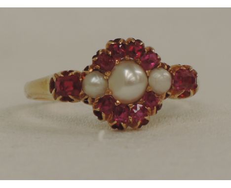 A lady's dress ring having a ruby and seed pearl cluster with baguette cut rubies to each shoulder on a yellow metal loop tes