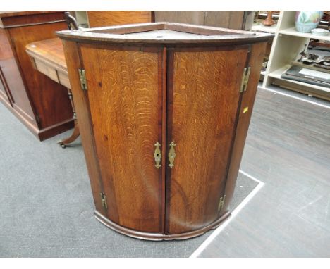 An early 19th century George III oak bow front corner cupboard having crossband decoration