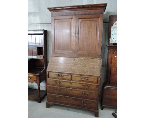An early 19th century oak bureau bookcase having cupboard doors, with crossband inlay over fall front bureau with drawer base