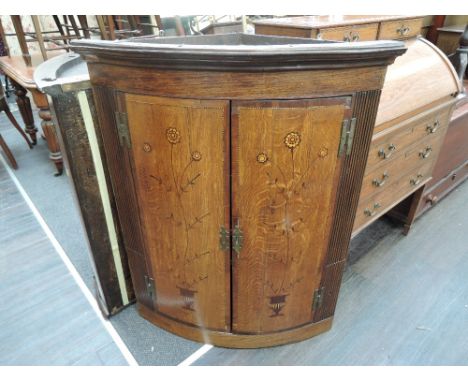 An early 19th century George III oak bow front corner cupboard having foliate inlay decoration