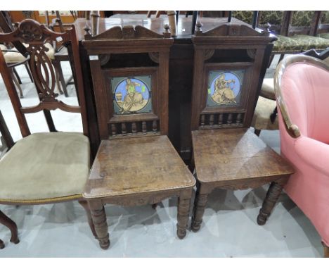 A pair of Victorian oak hall chairs of Gothic revival style having spindle and crest backs with inset Mintons ceramic tiles o