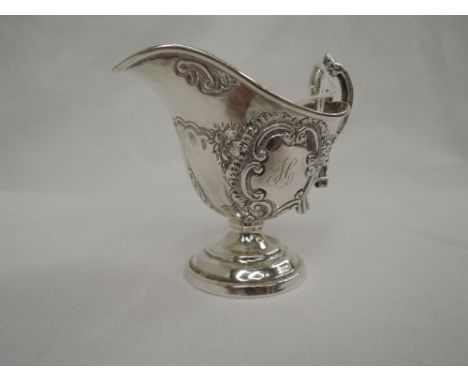 A Victorian silver cream jug having repousse decoration, architectural moulded handle and inscription to cartouche, Birmingha