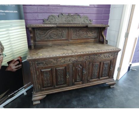 A late Victorian oak sideboard having extensive carved decoration with railed ledge back over triple cupboard on heavy bracke