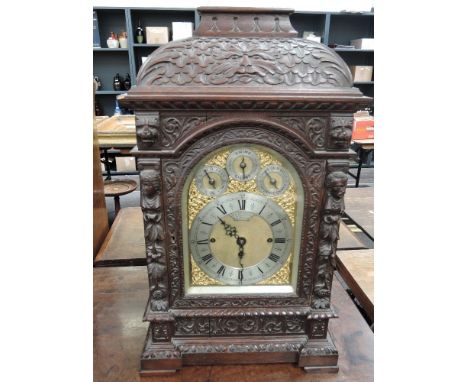 A late 19th century oak bracket clock having extensive carved foliate and mask decoration to case, with arched brass and silv