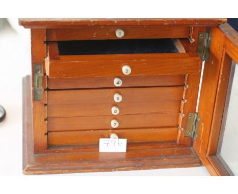 A COIN COLLECTORS CABINET. In a light wood with glazed front door, fitted with eight lined numbered drawers of uniform size. 