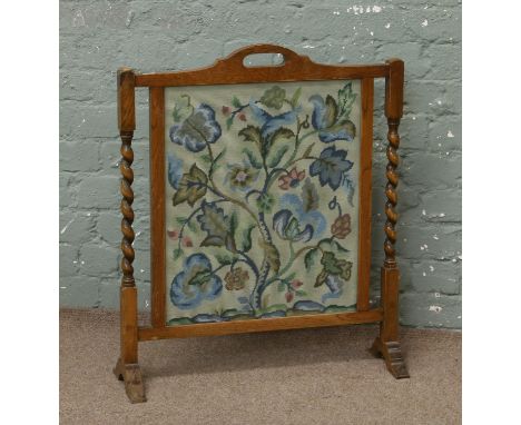 A vintage oak firescreen with floral embroidered panel, raised on barleytwist supports.