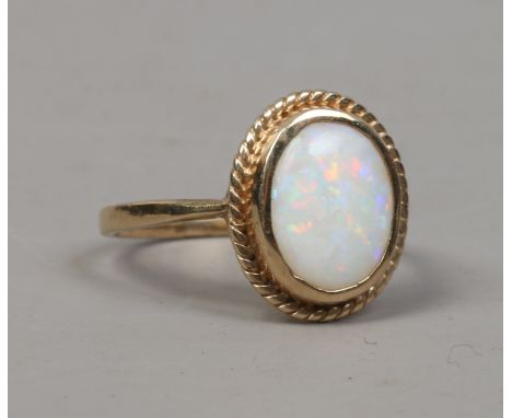 A 9ct gold opal dress ring with ovoid stone under a ropetwist border, size L.