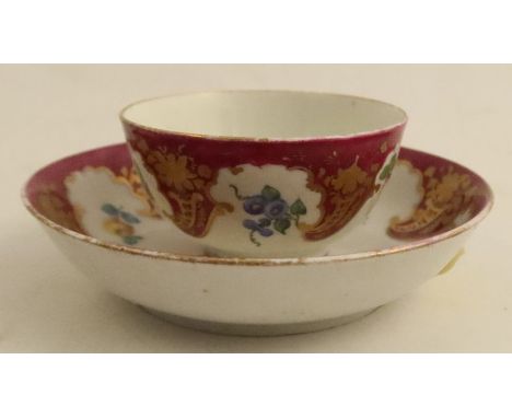 A Worcester tea bowl and saucer, later decorated with the Hope Edwards pattern of flowers, fruits and vegetable to a claret b
