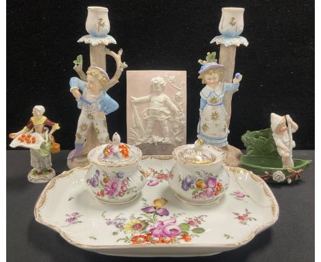 A Samson Paris porcelain figure, of a fruit seller, 10.5cm high; a pair of Continental bisque figural candlesticks, of a boy 