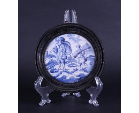 A framed earthenware tile, round with a decoration of two figures in a landscape. May be part of a larger tile. Dutch(?)Diam.
