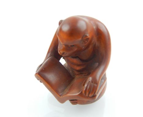A carved Japanese netsuke, in the form of a monkey reading a book. 