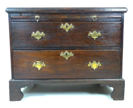 A Georgian oak chest of two long drawers, the top with unusual hinged front to shallow fitted compartment below, above brushi