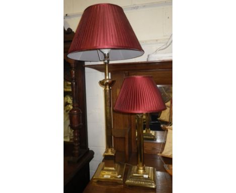 A brass Corinthian column table lamp with red pleated shade and another similar