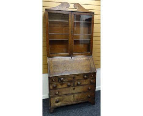 AN EARLY NINETEENTH CENTURY OAK BUREAU BOOKCASE having a two door glazed top with sloped front hinging to reveal an arrangeme