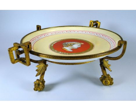 A CONTINENTAL PORCELAIN COMPORT on a gilt metal stand, the interior of the porcelain decorated with a Romanesque portrait & w
