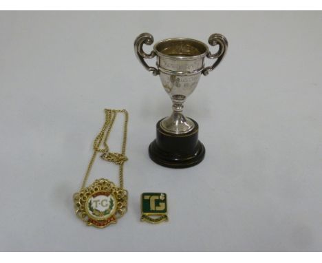 A miniature silver trophy cup, a gilt metal and enamel badge and another metal and enamel badge