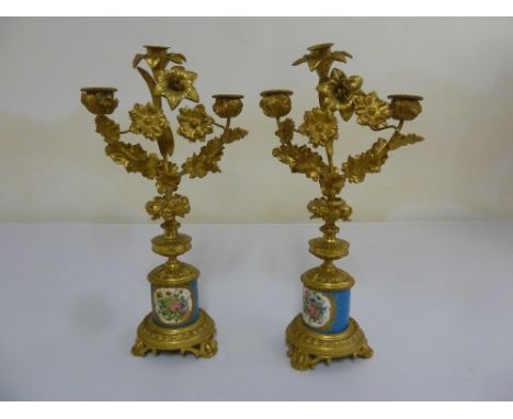 A pair of gilded metal and porcelain two light candelabra, leaf chased branches on cylindrical base