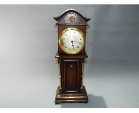 An oak cased mantle clock in a form of a long case clock with key approximate height 40 cm x 13 cm x 9 cm.