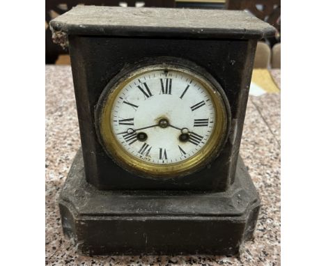 A black slate mantle clock, with a rectangular top above a circular dial with Roman numerals and a plinth base 22cm high