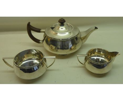 A silver circular three piece Teaset of compressed form, the teapot with stained wood handle and lift, Birmingham, 1930, make