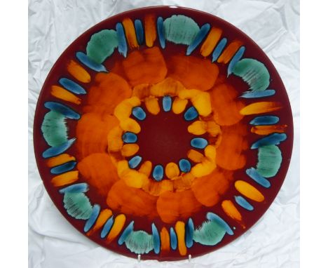A Poole Pottery Charger decorated in orange, yellow, blue, etc., 16" (41cms) diameter.