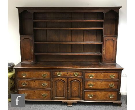 A George III crossbanded oak dresser, the panelled cupboard back on a base enclosed by a pair fielded arch fan paterae inlaid
