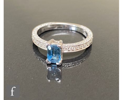 A hallmarked 18ct white gold sapphire and diamond ring, central emerald cut claw set sapphire, length 6mm, to a diamond encru