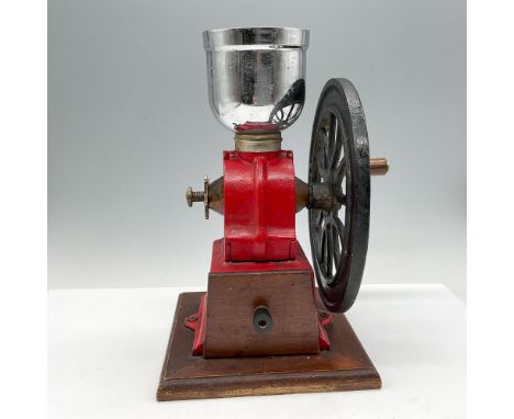 Red cast iron grinder with black turn wheel with wooden handle and drawer. Top open aluminum cup holds beans. Grinder is moun