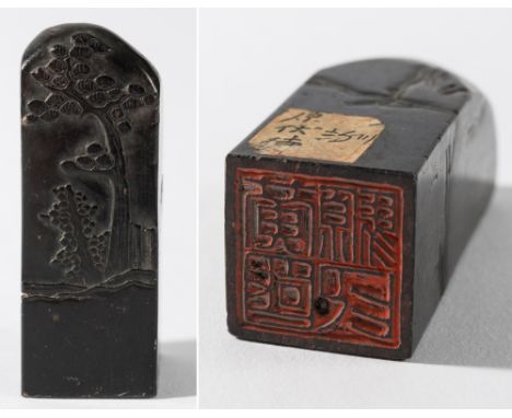 A Chinese black jade seal: of square section carved with rockwork, a pine tree and a shrub, the base with four-character seal