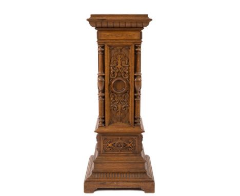 An Edwardian carved oak square pedestal:, the stepped top with a moulded and dentil edge, the panelled sides with blind fret 