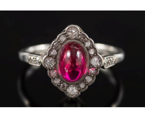 A synthetic ruby and diamond, oval cluster ring:, the central cabochon synthetic ruby within a surround of brilliant and sing