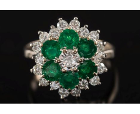 An emerald and diamond circular cluster ring: the central, brilliant-cut diamond estimated to weigh 0.25ct, within a surround