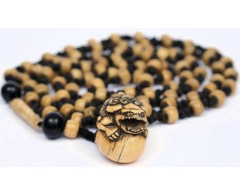 An early 20th century Japanese bone necklace: knotted with ivory netsuke depicting with lion dog holding a ball, some damage.