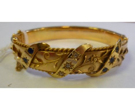 An Edwardian 9ct gold hollow, hinged bangle, overlaid in filigree wirework, three parallel, scrolled ribbons set with sapphir