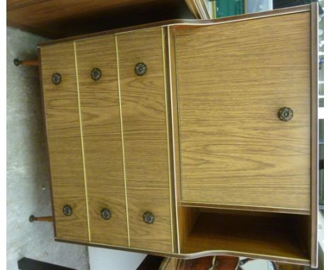 A 1960s teak laminate finished desk, the offset fall front enclosing a fitted interior, over three long drawers, raised on tu