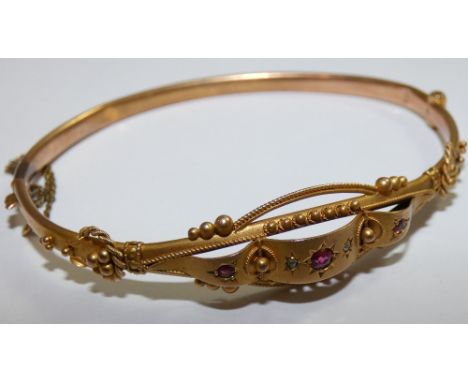 An Edwardian 9ct gold bangle, the panel front set with red paste and diamond chips, weight 5.5 gms.