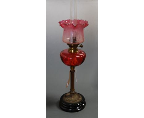 A late Victorian oil lamp, having an etched and cranberry tinted frilled glass shade above a cranberry glass font, to a brass