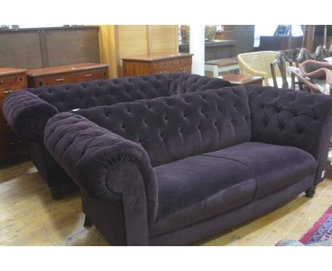 A pair of modern two seater Chesterfield button back sofas upholstered in plum plush fabric, raised on turned tapered support
