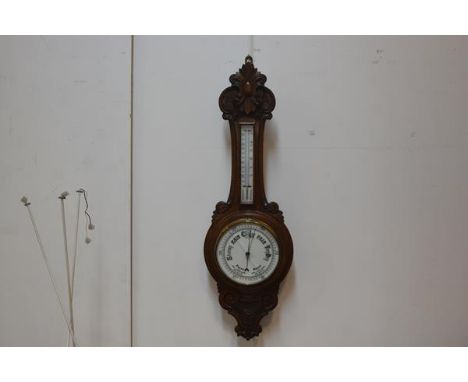 An Edwardian carved oak aneroid barometer and thermometer with enamelled dial. 90cm by 30cm