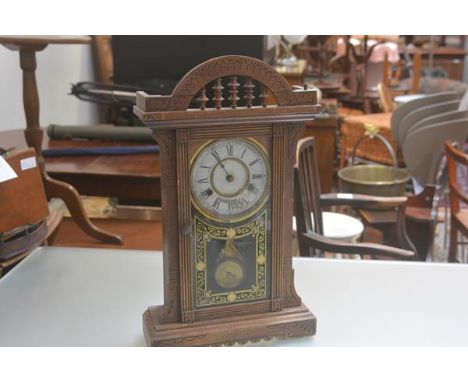 A 19thc American treen gingerbread style mantle clock with pedimented top and enamel dial, with glass inset panel door, compl
